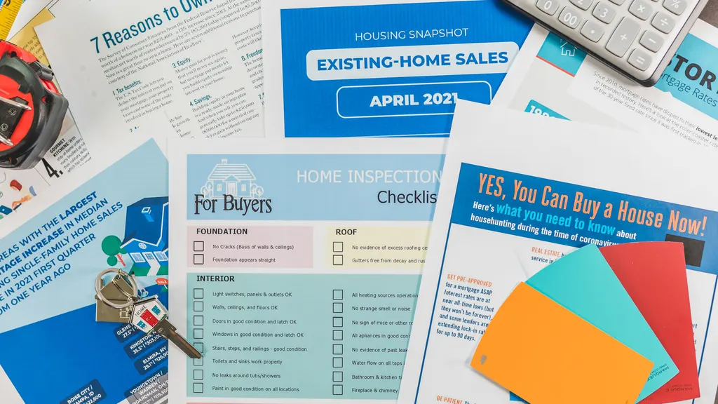 Printed real estate flyers and checklists laid out on a desk beside a set of house keys.
